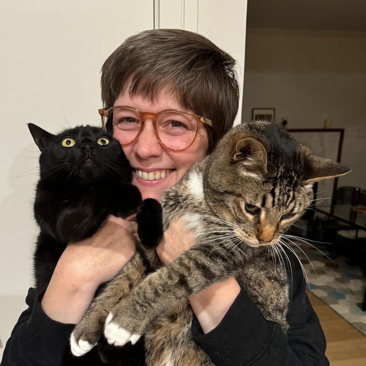 Carrie with two cats: a black cat named Olive, and a gray tabby named K2.